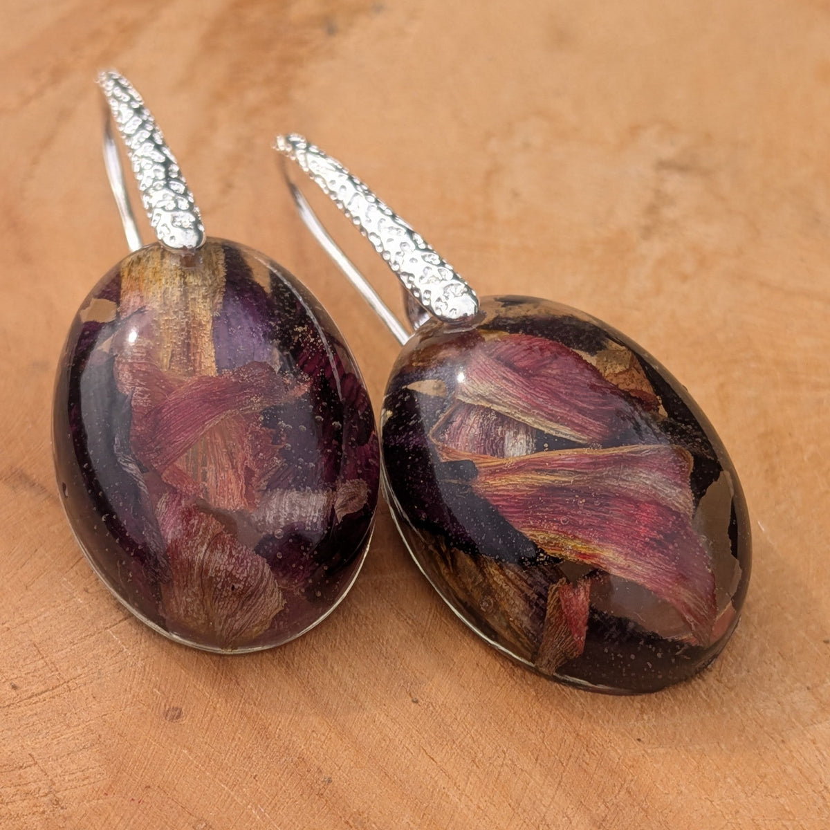 Handmade tulip petal resin earrings 25x18mm oval cabochon on textured silver hooks side view on wood – EL-Creations