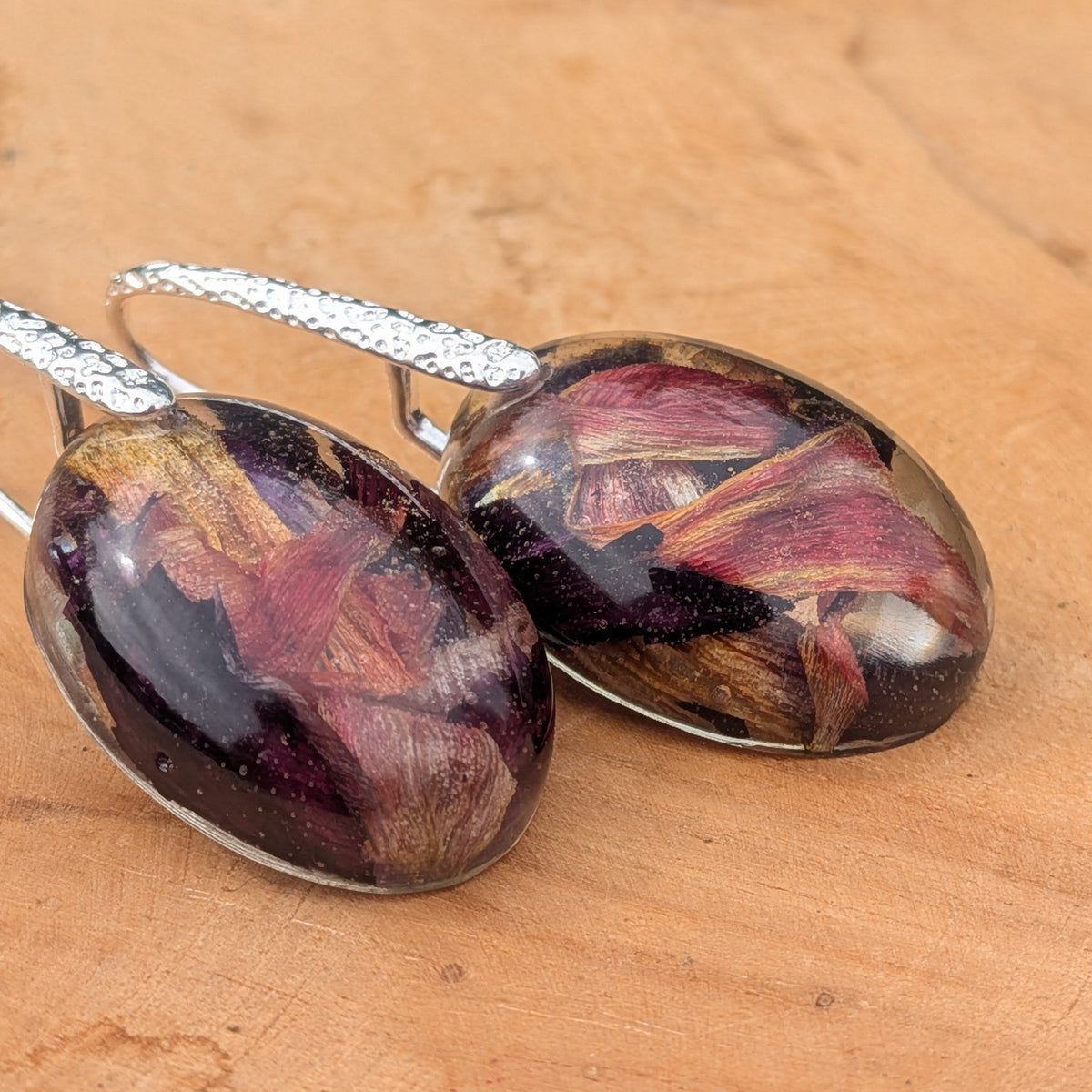 Resin botanical drop earrings with dried tulip petals in burgundy gold purple angled view on wood – EL-Creations