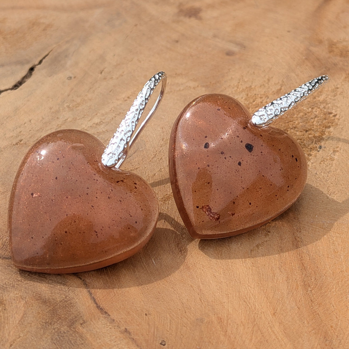 Chunky brown resin heart drop earrings with copper flakes on textured silver hooks front view on driftwood – EL-Creations