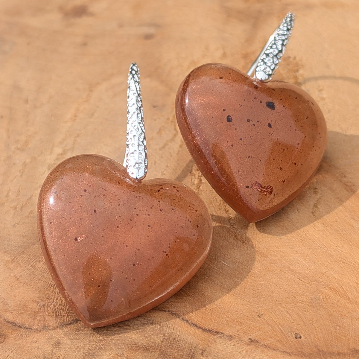 Handmade brown resin heart earrings 20mm diameter with hammered silver hooks side view on driftwood – EL-Creations