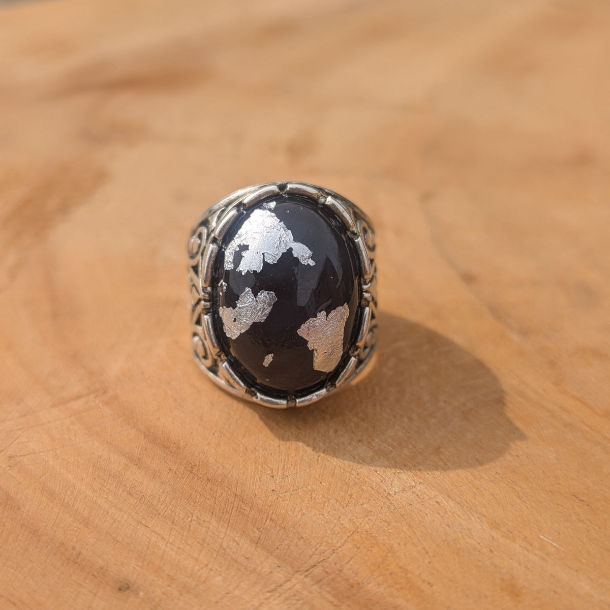 Gothic unisex statement ring black resin oval cabochon with silver flakes front view on wood – EL-Creations