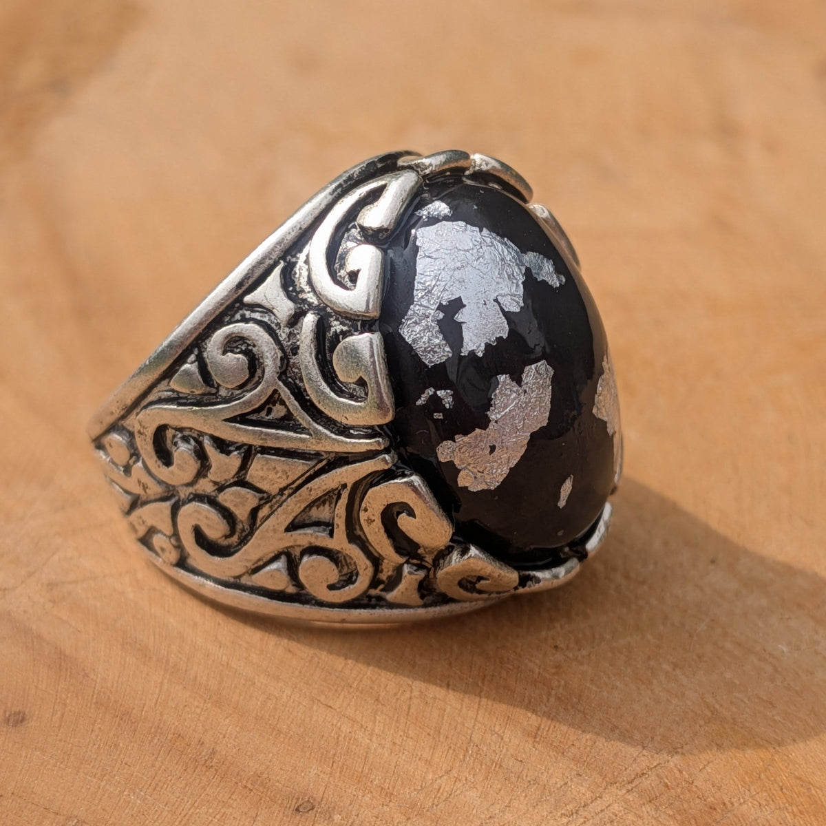 Black resin ring with silver flakes top view showing full filigree band detail on wood – EL-Creations