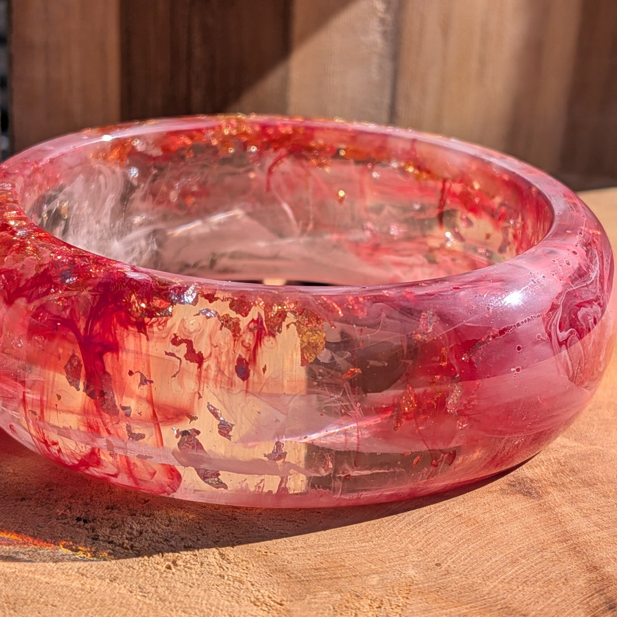 Handmade rose crimson resin bangle standing upright showing swirling pigment and metallic flakes on wood – EL-Creations