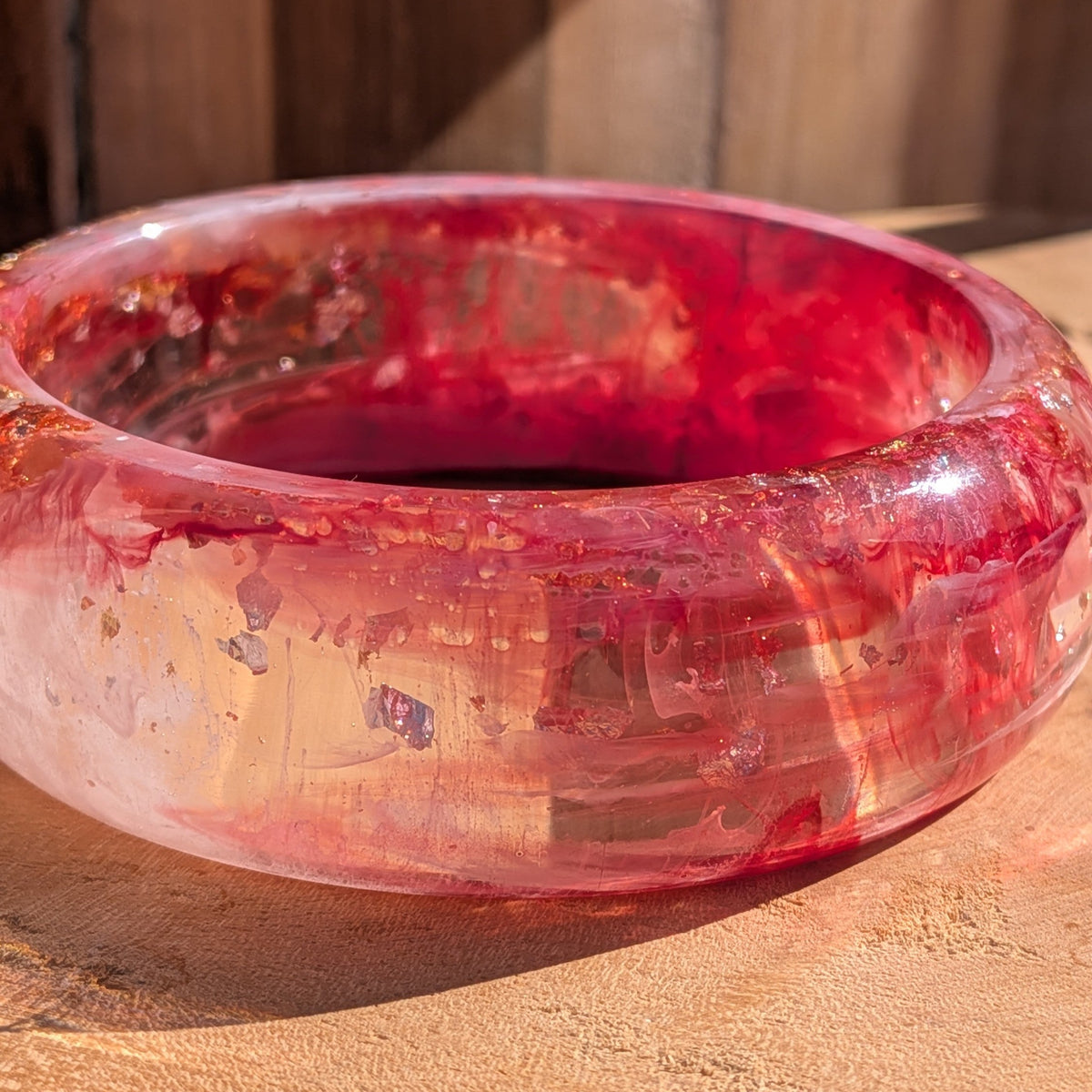 Pink red resin dome bangle angled view showing gold copper silver flakes suspended in clear resin on wood – EL-Creations