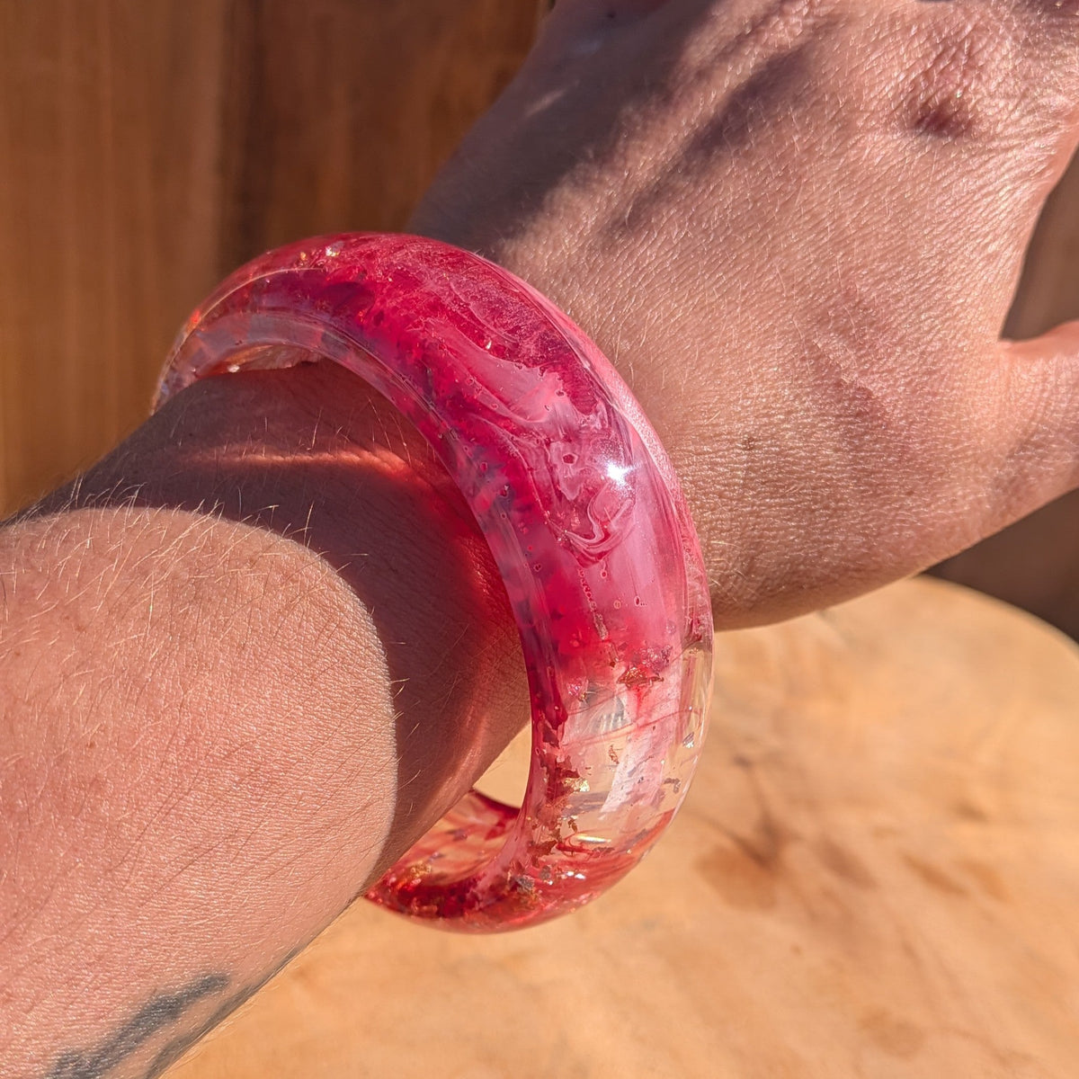 Handmade rose resin bangle with crimson swirls and gold flakes worn on wrist front view outdoor – EL-Creations