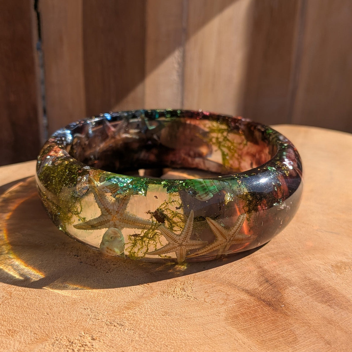 Ocean resin statement bangle standing upright showing real dried starfish and sea moss inclusions on wooden surface – EL-Creations