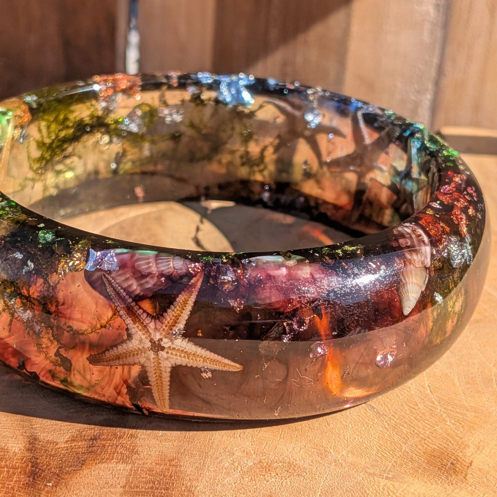 Real starfish resin bangle close-up showing dried starfish and spiral seashells preserved in clear resin on wood – EL-Creations