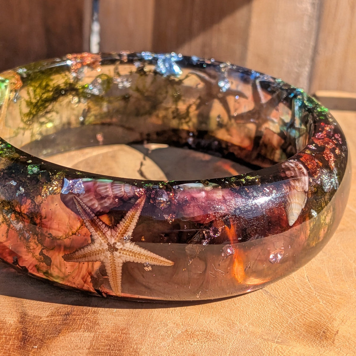 Real starfish resin bangle close-up showing dried starfish and spiral seashells preserved in clear resin on wood – EL-Creations