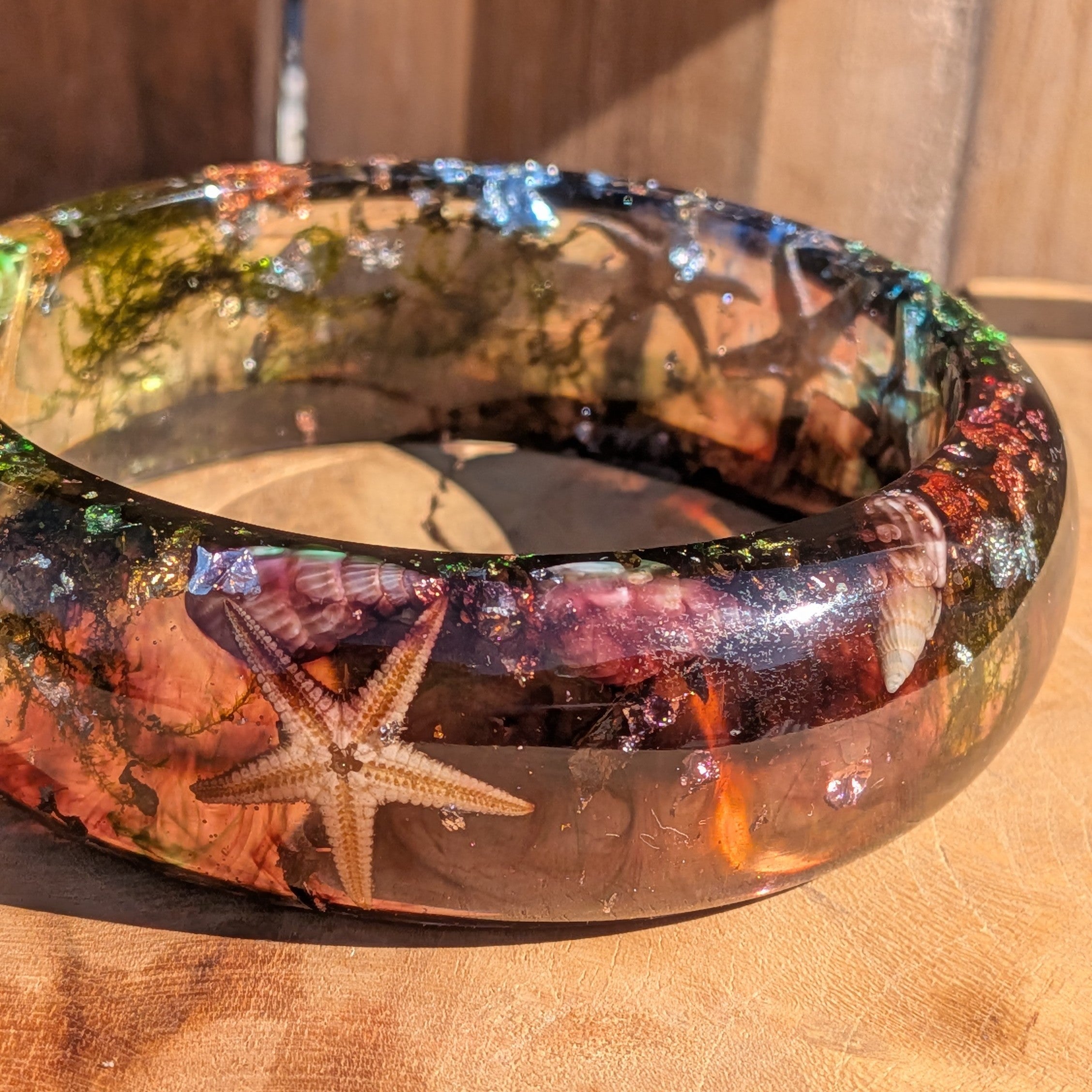 Real starfish resin bangle close-up showing dried starfish and spiral seashells preserved in clear resin on wood – EL-Creations