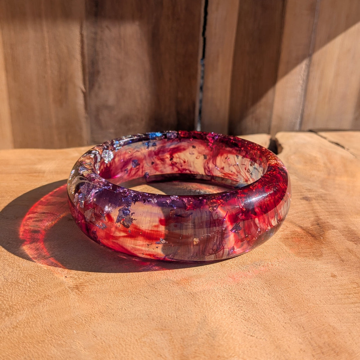 Handmade red and purple resin bangle with silver gold copper flakes standing upright on wooden surface – EL-Creations