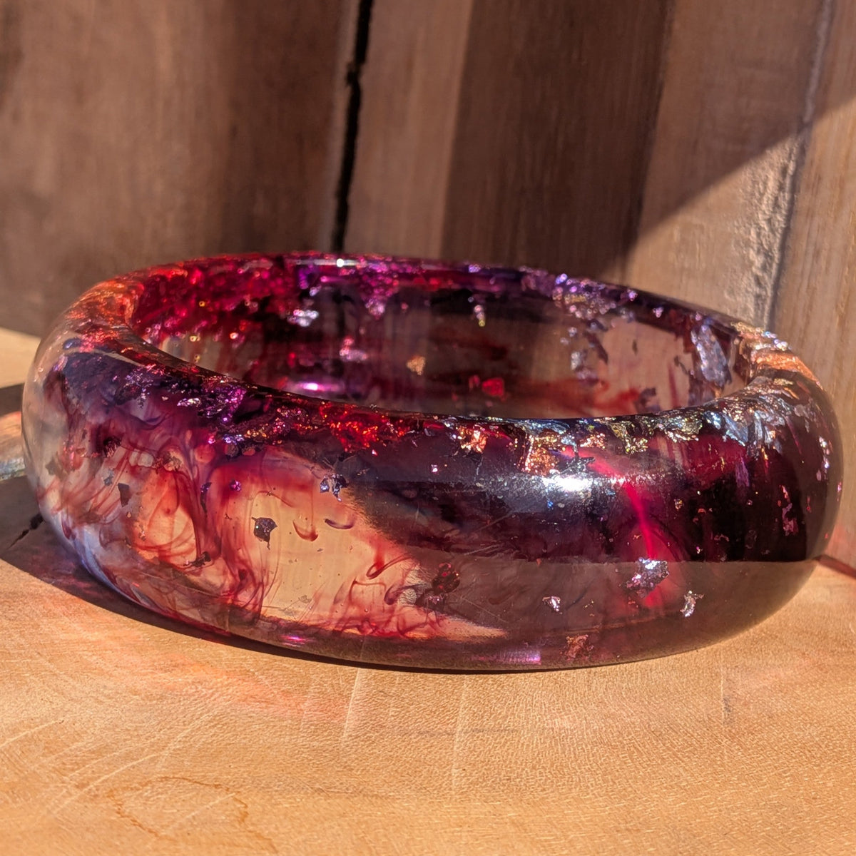 Red purple resin bangle close-up showing silver gold copper flakes suspended in clear resin on wood – EL-Creations