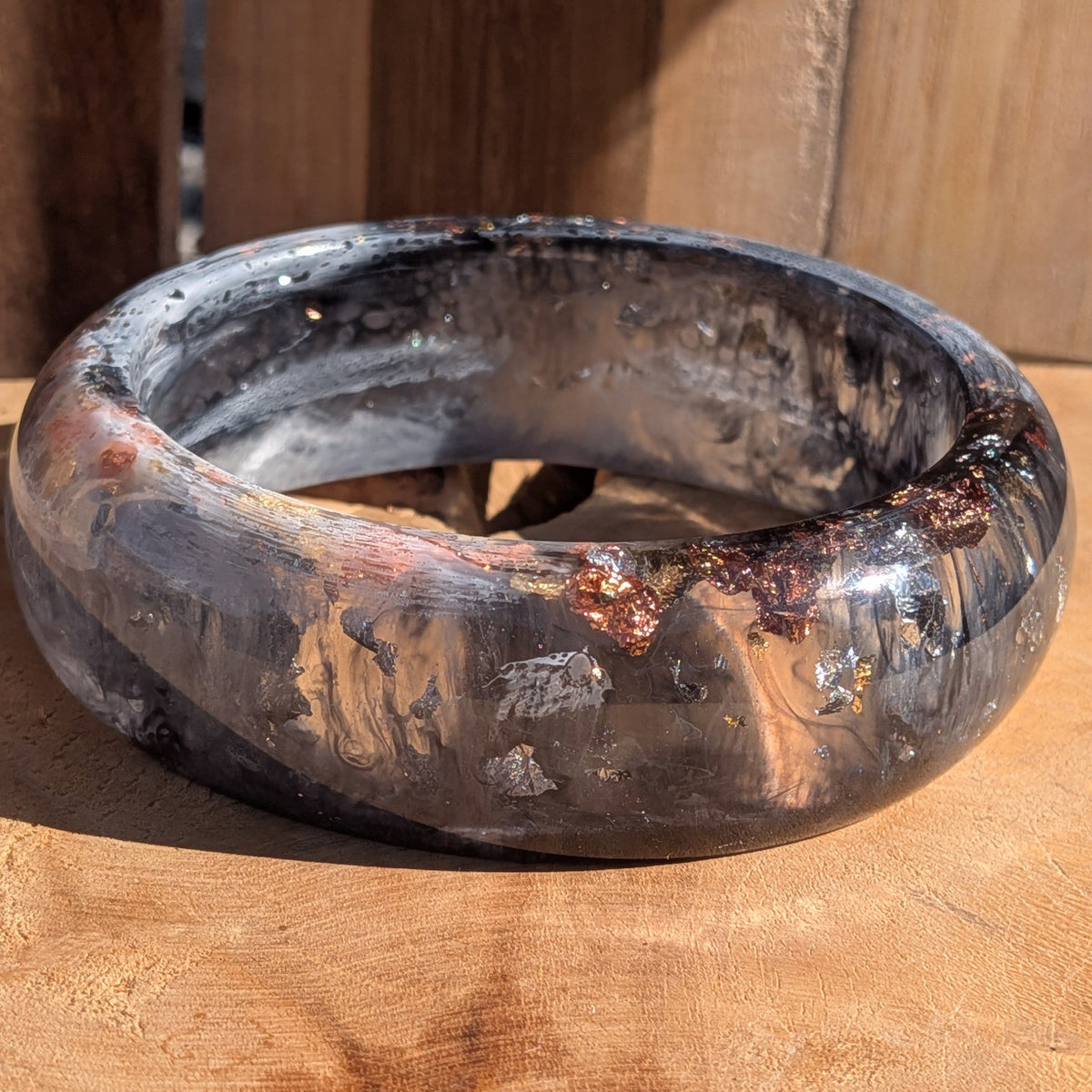 Handmade resin bangle black and white with gold silver copper flakes close-up showing depth on wood – EL-Creations