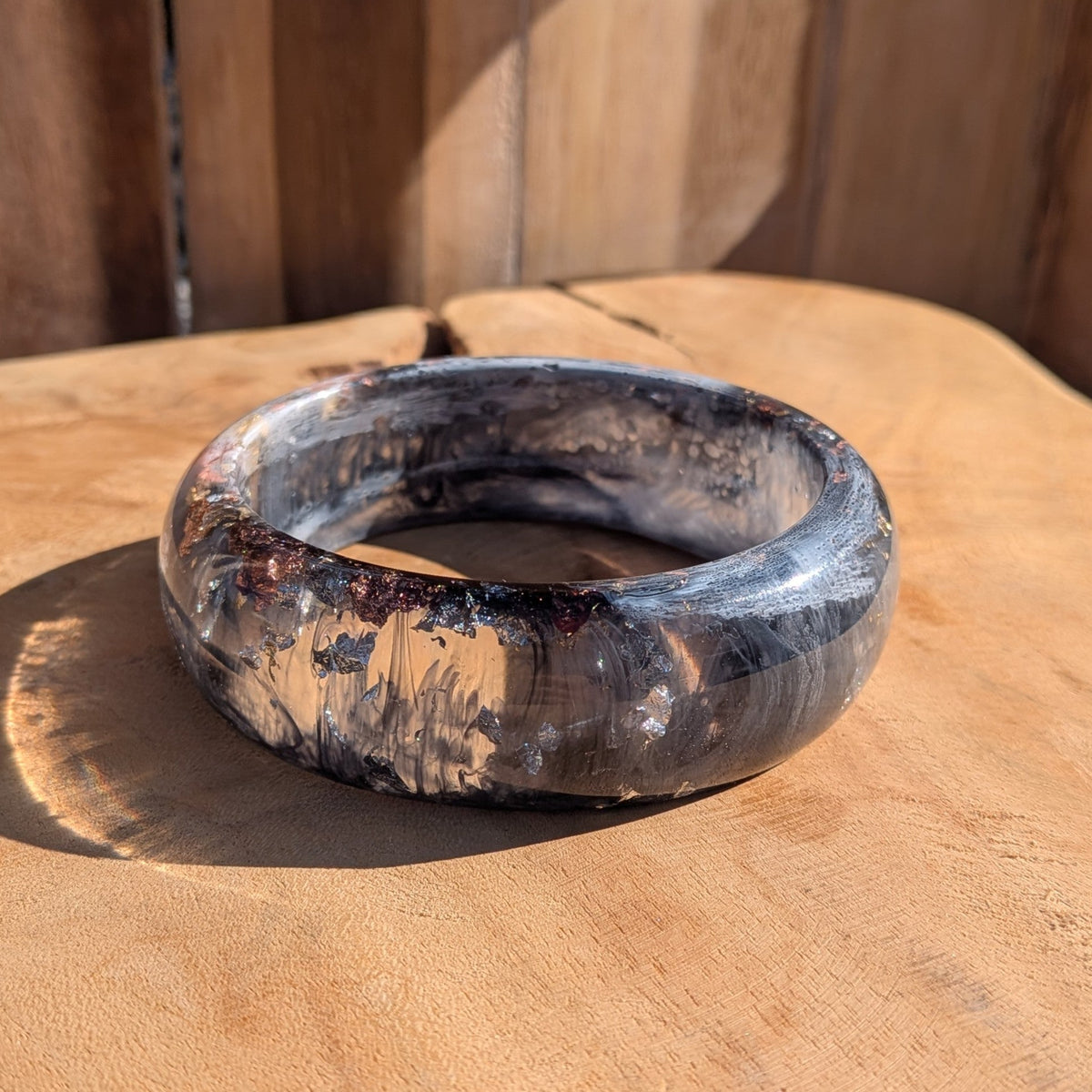Handmade black white resin bangle flat lay on wooden surface showing swirling pigment and metallic flakes – EL-Creations
