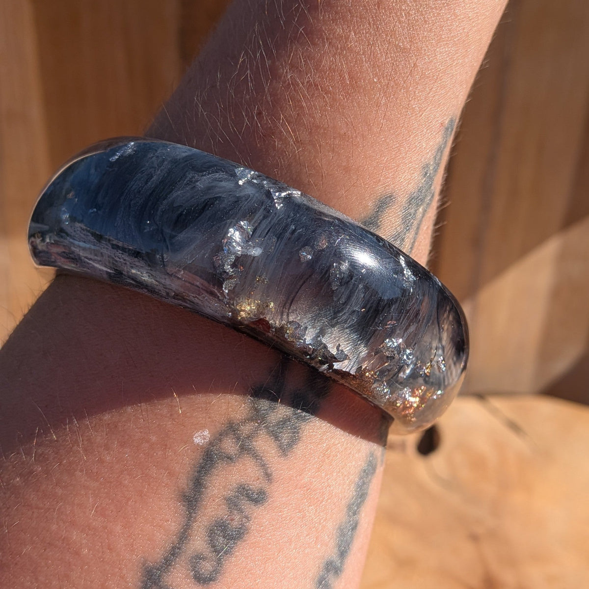 Chunky resin bangle black and white pigment swirls with gold copper silver flakes angled view on wood – EL-Creations