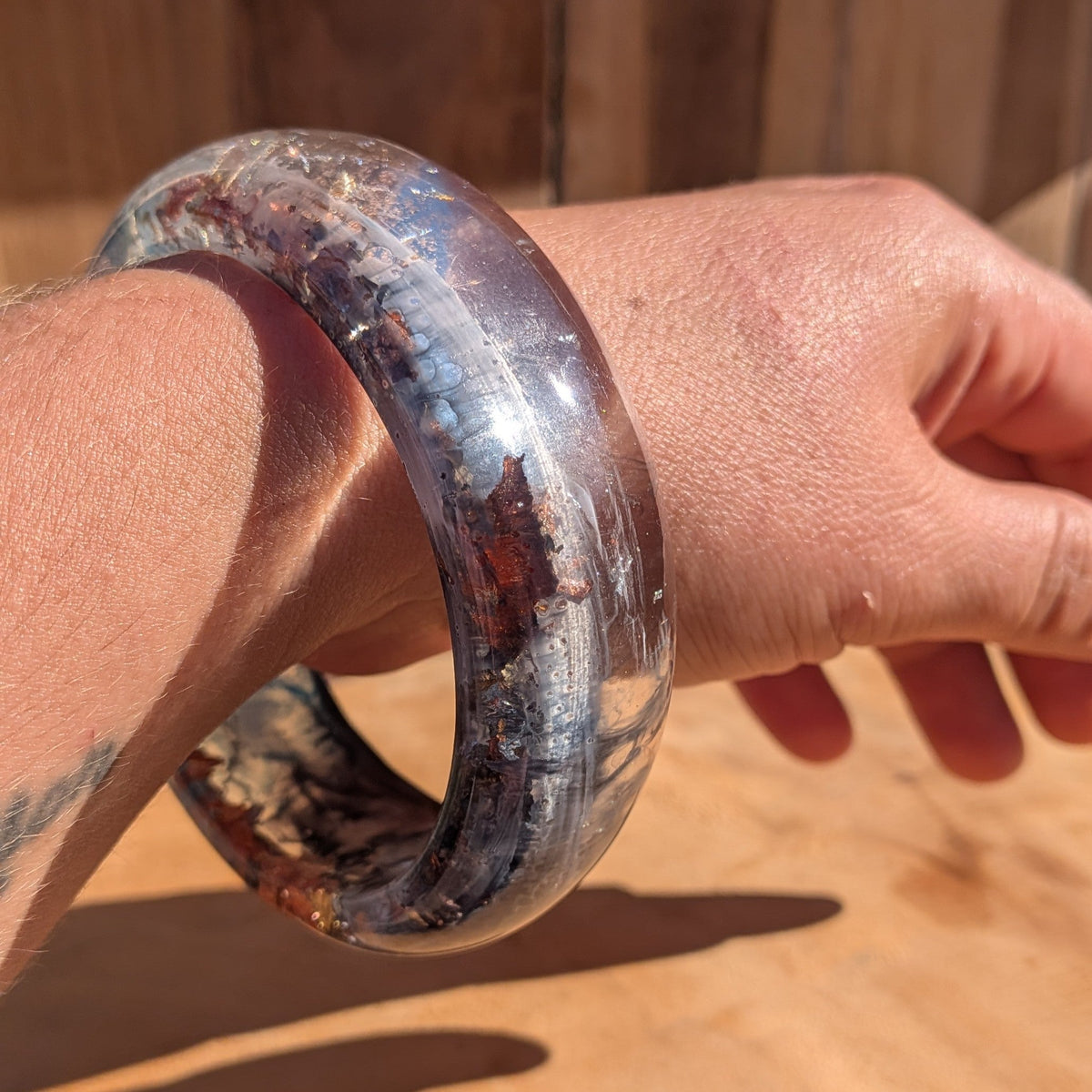 Wide blue resin bangle flat lay on driftwood showing full swirling pigment and metallic flake detail – EL-Creations