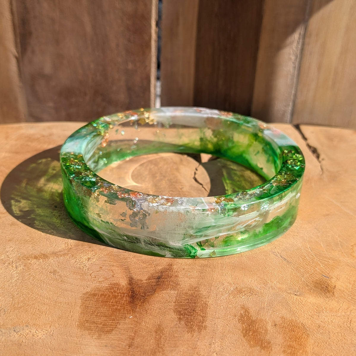 Green resin statement bangle standing upright showing swirling pigment and metallic flakes on wood – EL-Creations