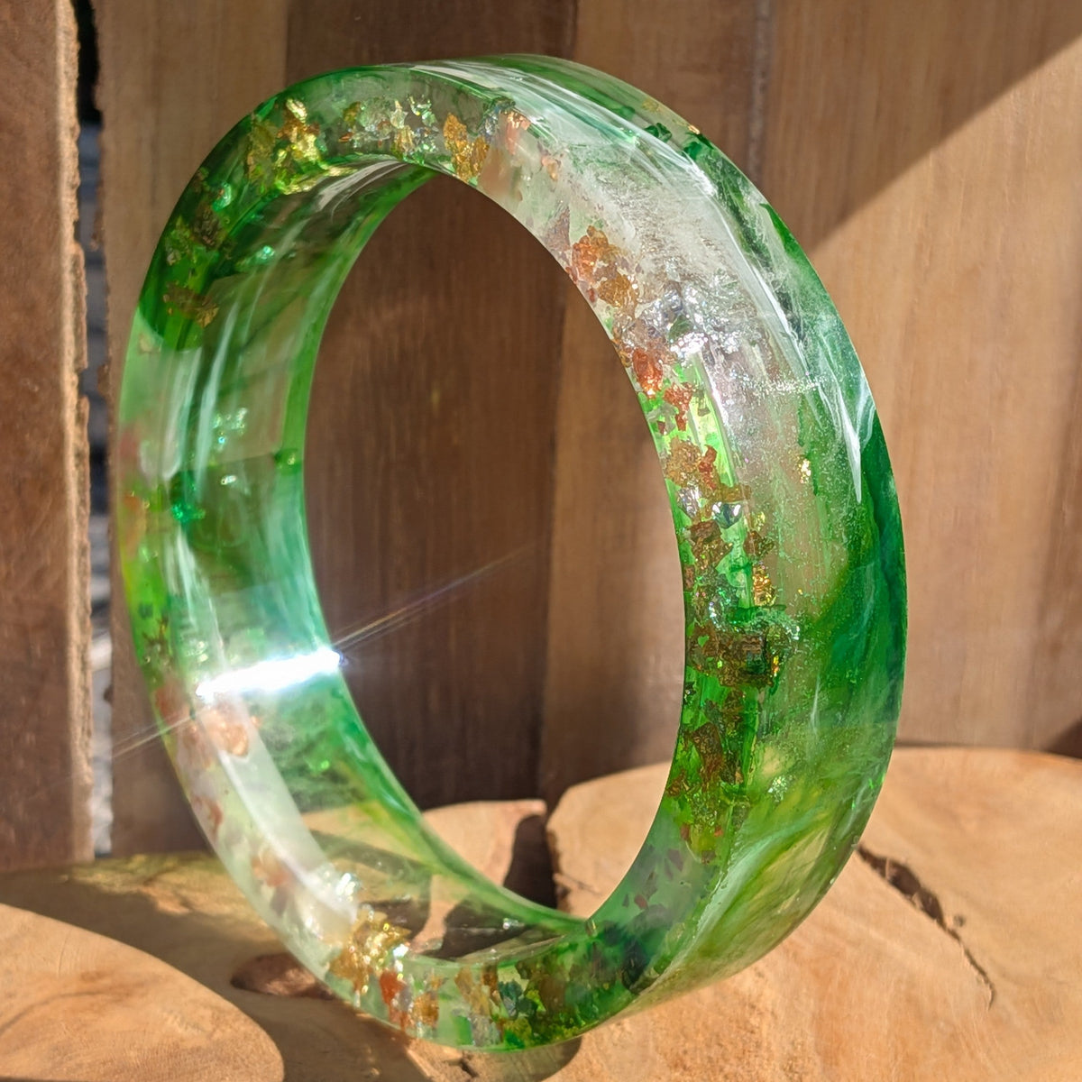 Handmade resin bangle with emerald green pigment and gold flakes worn on wrist close-up outdoor – EL-Creations