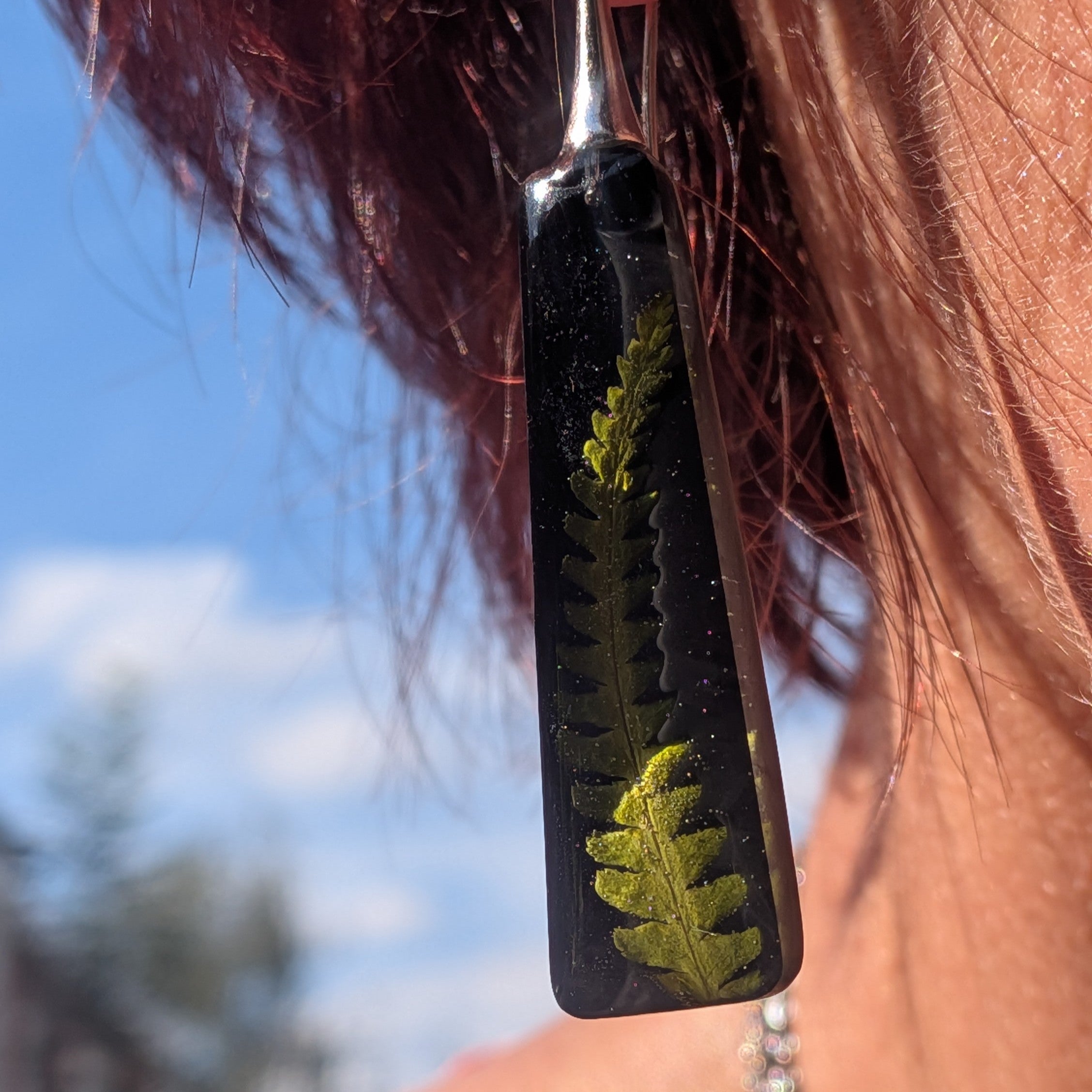 Black resin dangle earrings with real fern frond on wooden surface – close-up top view – EL-Creations