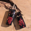 Black resin earrings with dried red flowers – leaning against driftwood in sunlight – EL-Creations