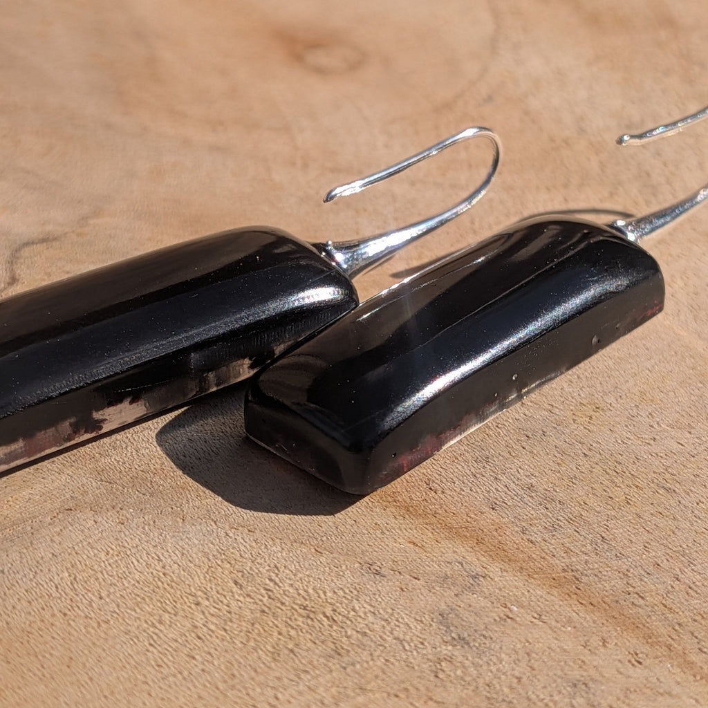 Black resin rectangular earrings with red and white dried flowers – side view against wooden wall – EL-Creations