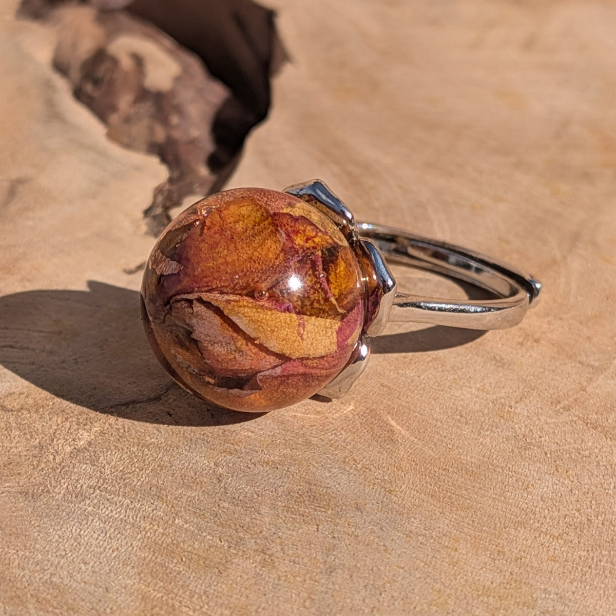 Clear resin globe ring with dried rose petals and copper shimmer, silver band, displayed on sandy surface – EL-Creations
