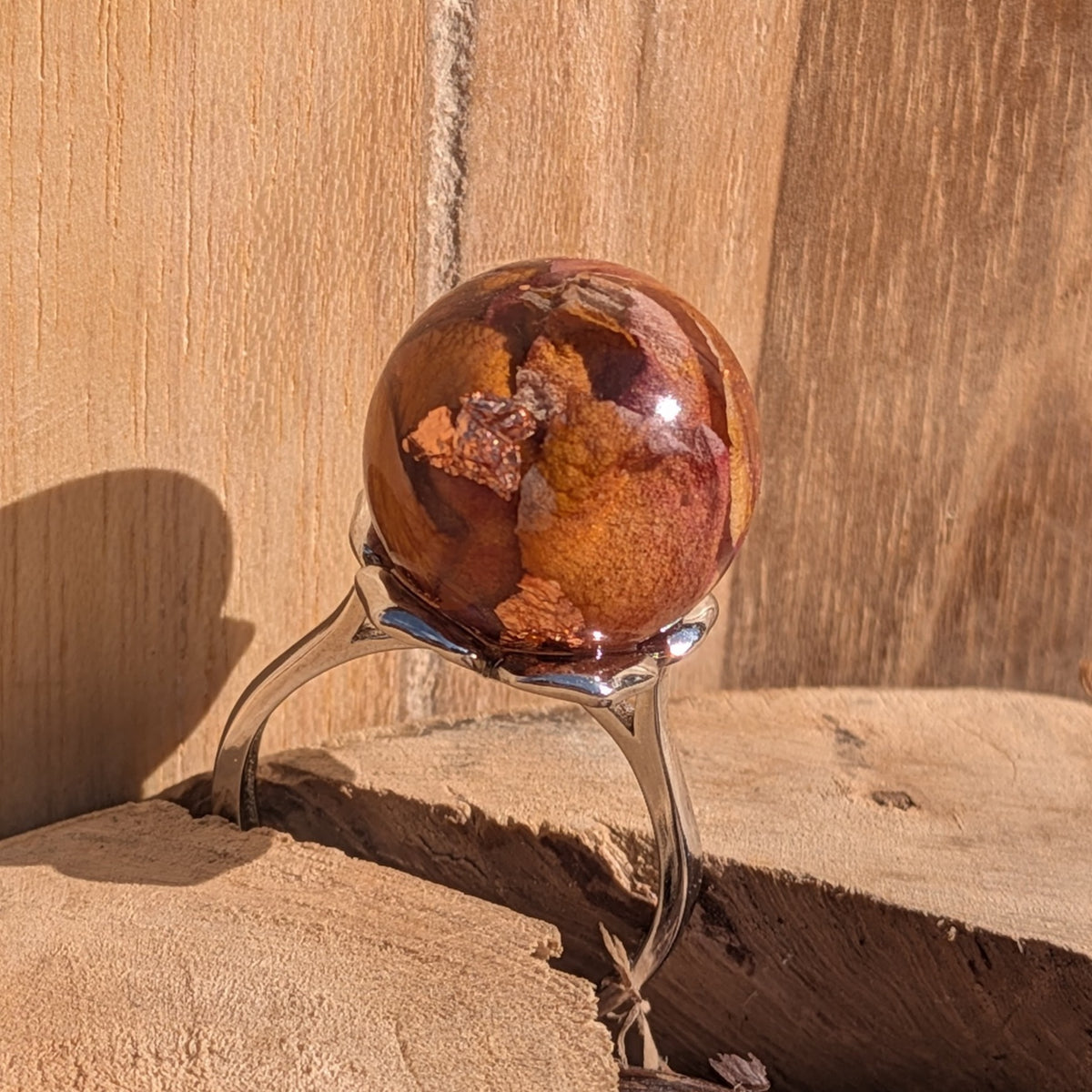 Resin globe ring with real rose petals and copper flakes, full view of silver adjustable band on wooden surface – EL-Creations