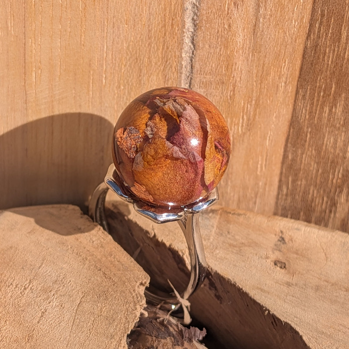 Top view of handmade rose petal resin sphere ring with copper flakes, silver adjustable band on rustic wood – EL-Creations