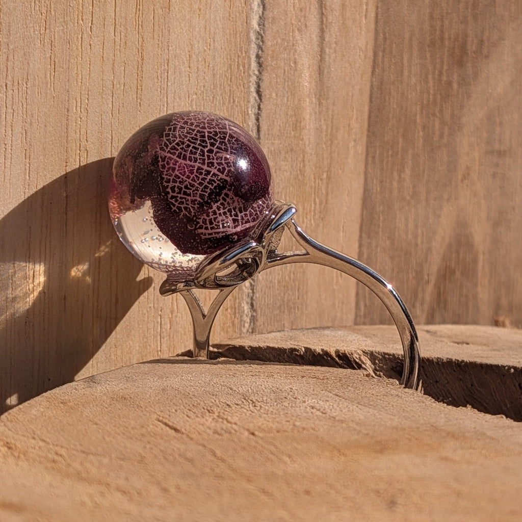 Clear resin globe ring with dried rose petals and skeleton leaf on wooden surface – side view – EL-Creations