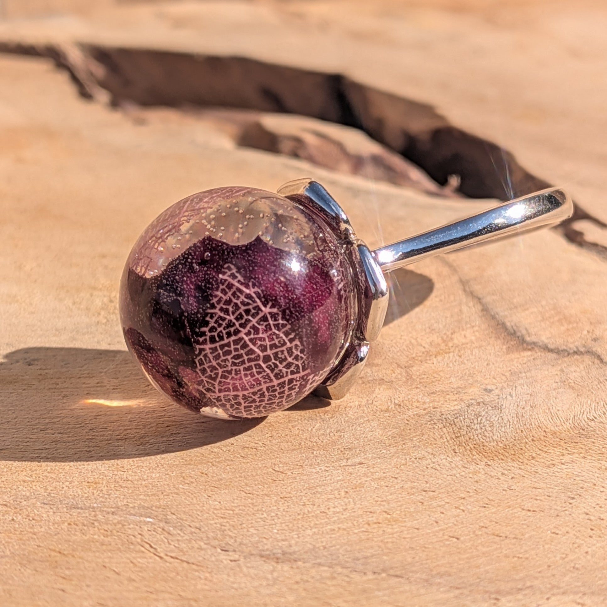 Globe resin ring with rose petals and skeleton leaf – top view on wooden surface – EL-Creations