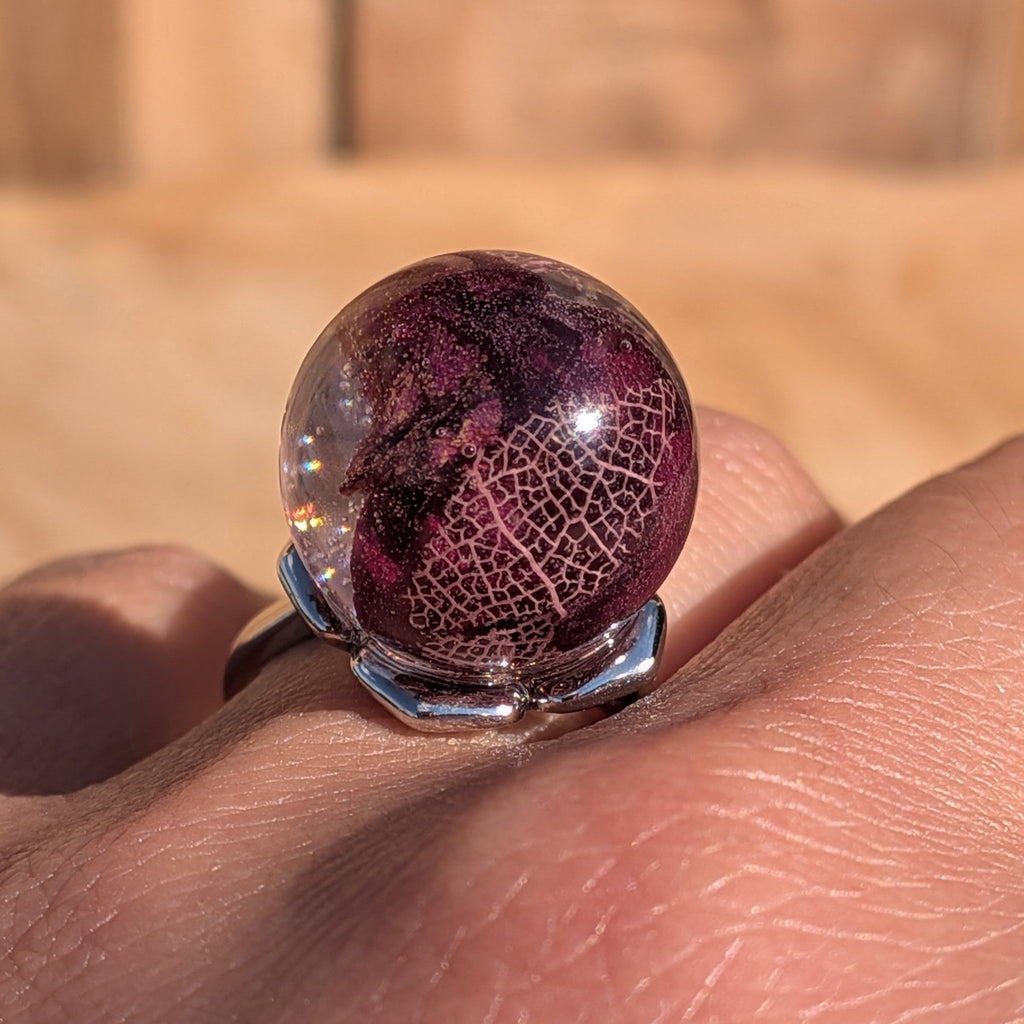 Dark burgundy resin ring with rose petals and skeleton leaf worn on finger – wooden background – EL-Creations