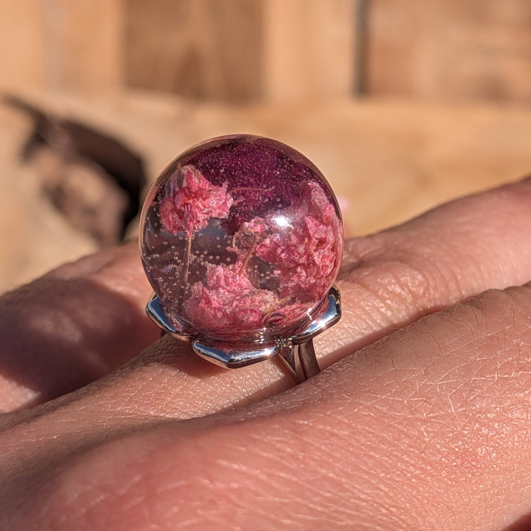 Clear resin globe ring with baby's breath and rose petals on silver adjustable band worn on finger in sunlight – EL-Creations