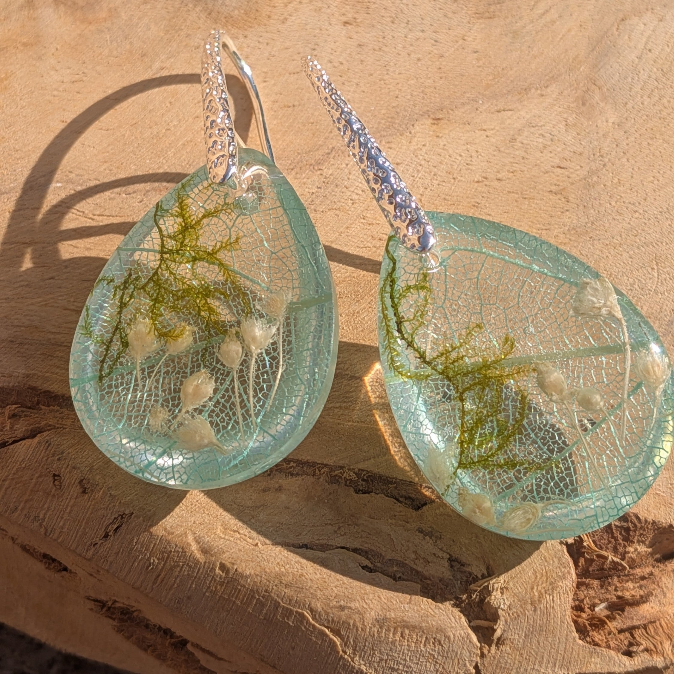Skeleton leaf resin teardrop earrings close-up on wood showing lace texture and white wildflowers – EL-Creations