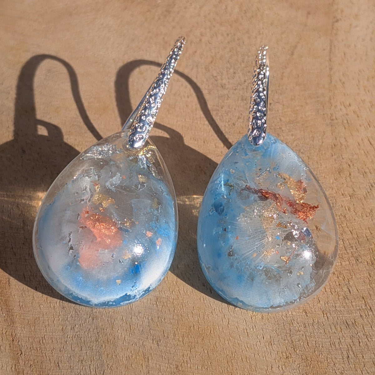 Angled view of glossy blue and white resin earrings with silver hooks, EL-Creations