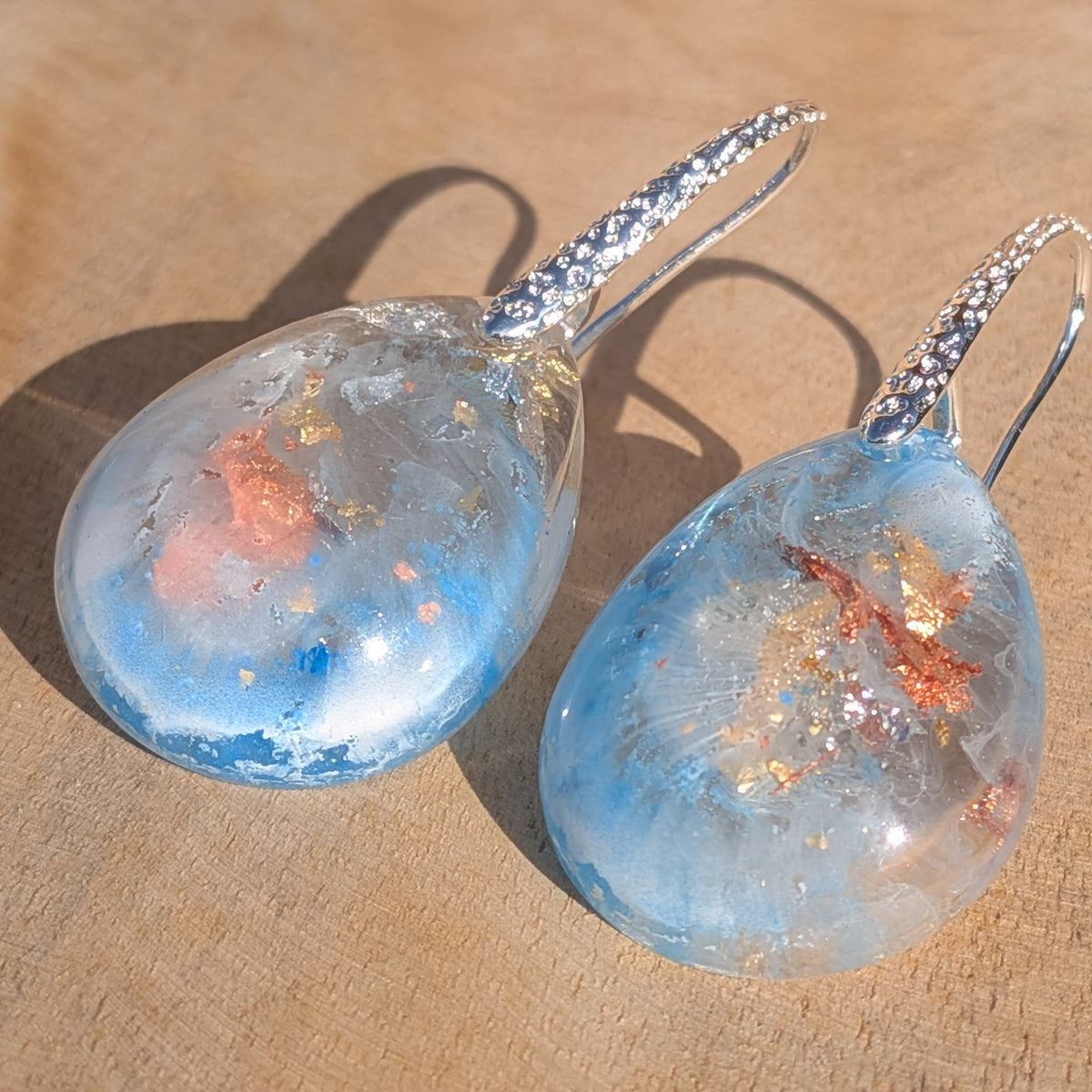 Close-up of abstract blue and white teardrop earrings with copper flakes, EL-Creations