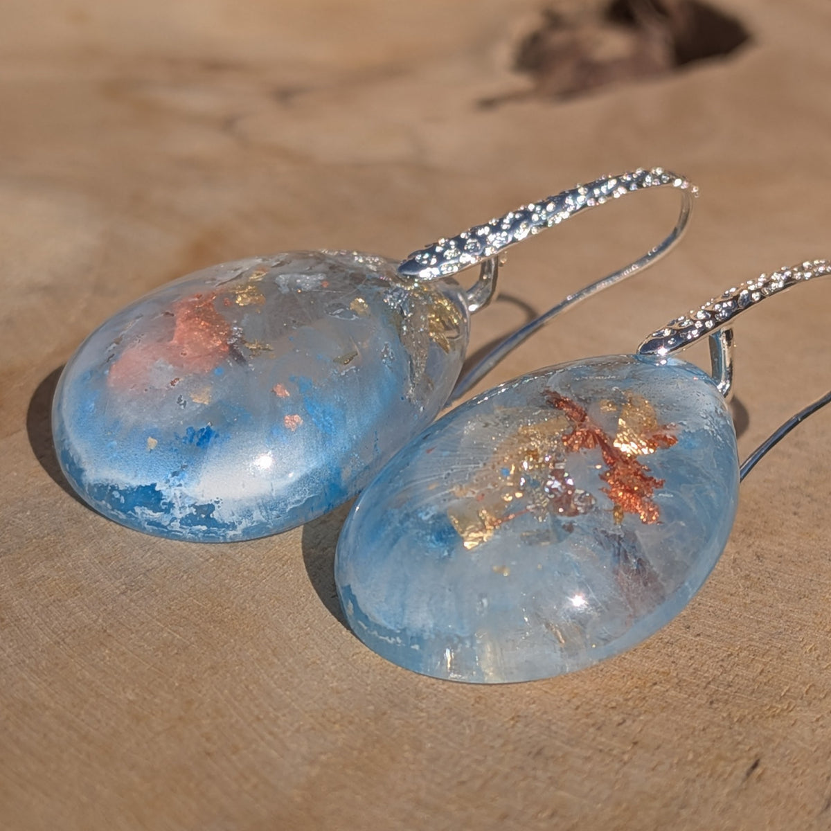 Low-angle view of glossy abstract blue resin earrings with white patterns, EL-Creations
