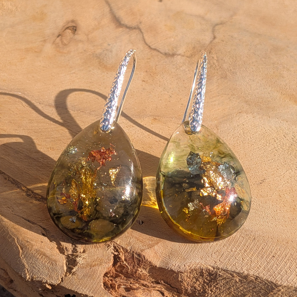 Pair of olive green and amber resin drop earrings displayed in sunlight on wood, EL-Creations