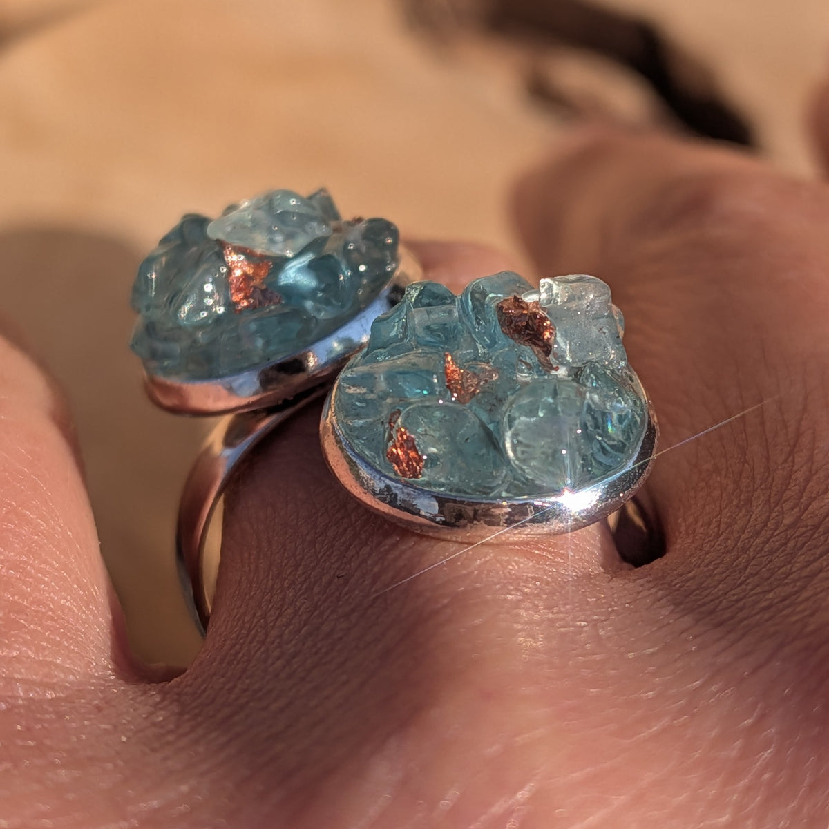 Close-up of the blue topaz double cluster ring worn on a finger in sunlight, EL-Creations