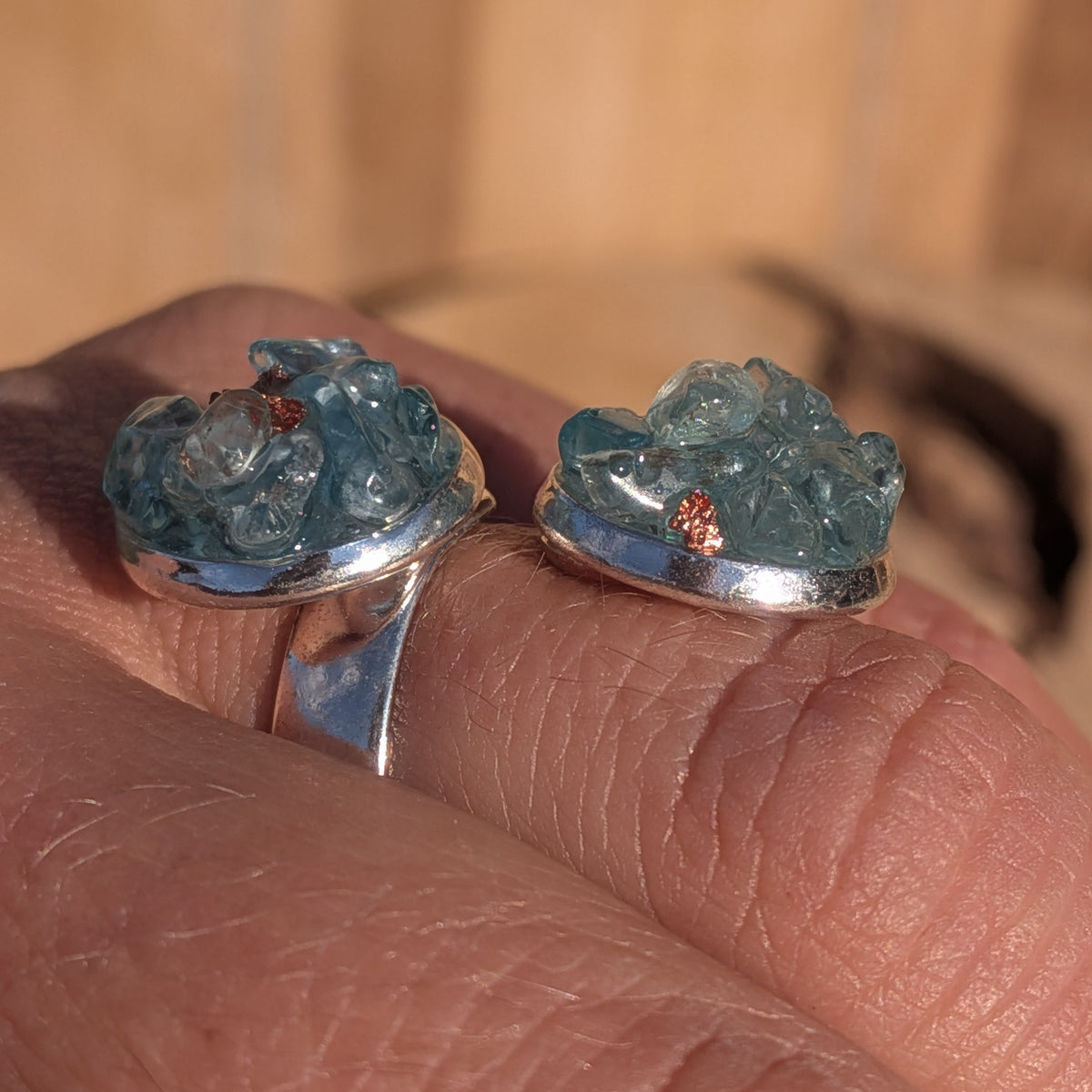 Low side view of the blue topaz ring showing raised stones above both settings, EL-Creations