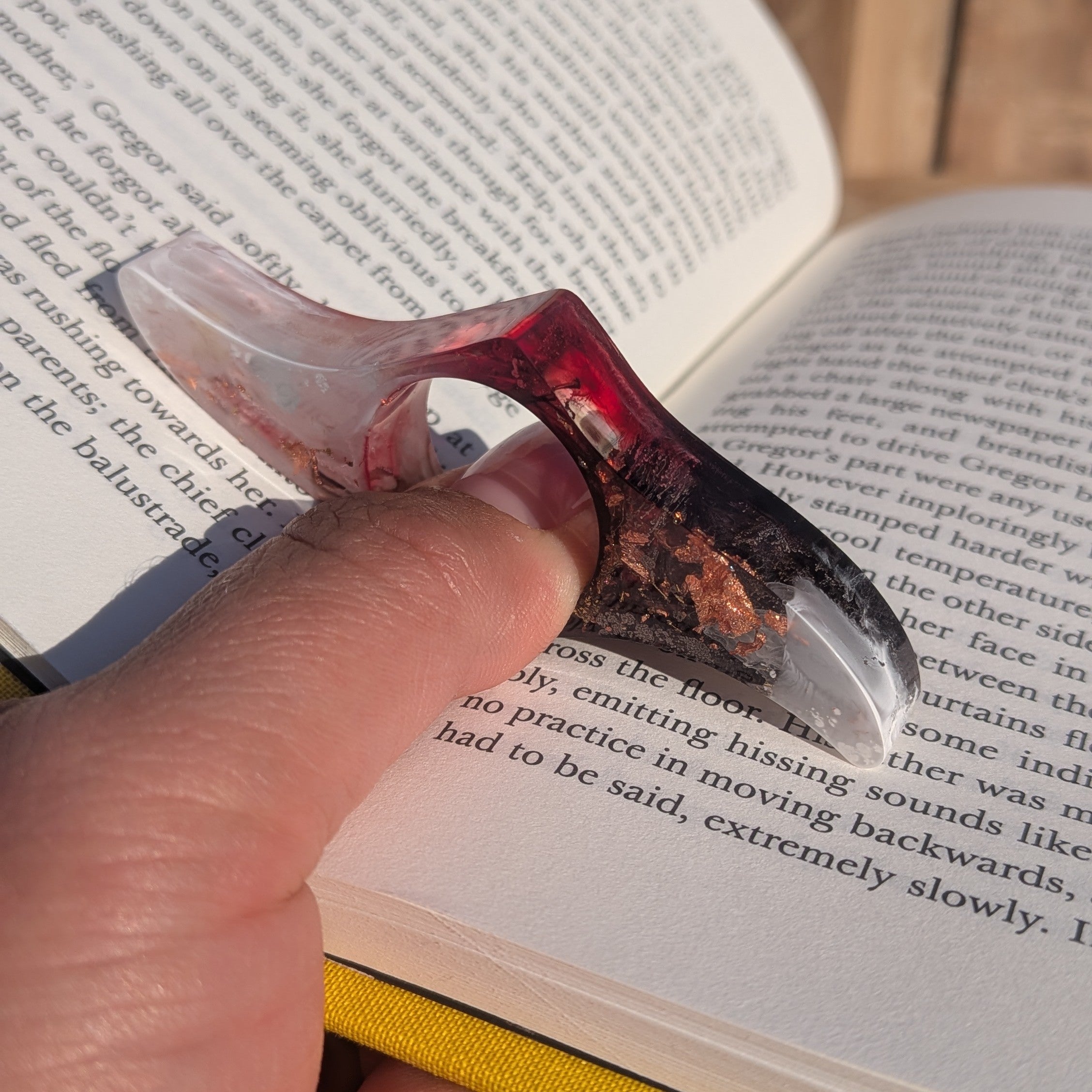 Resin reading ring with copper flakes in use on thumb over open book – close-up view – EL-Creations