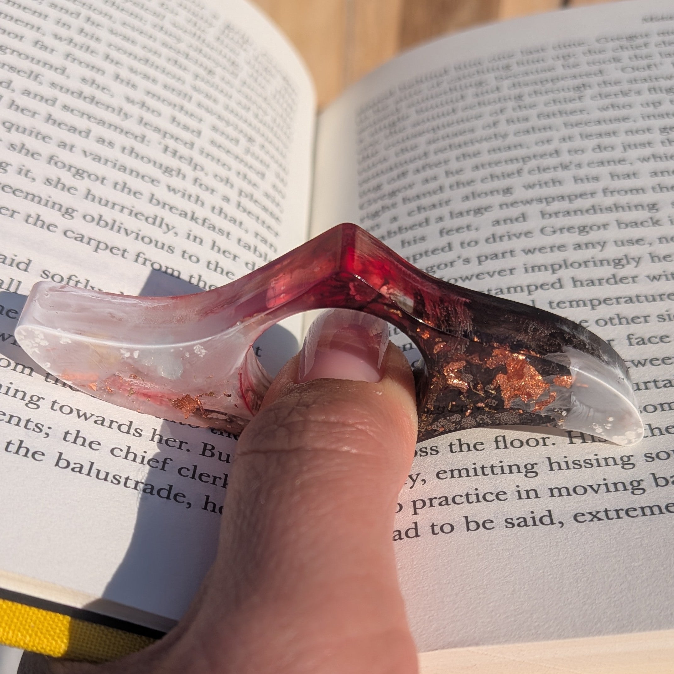Resin book ring with copper flakes held on thumb over open book pages – EL-Creations
