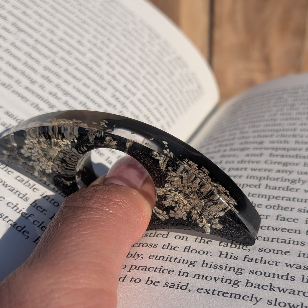 Black resin book ring with real Queen Anne's Lace flowers – angled view on sandy wooden surface – EL-Creations