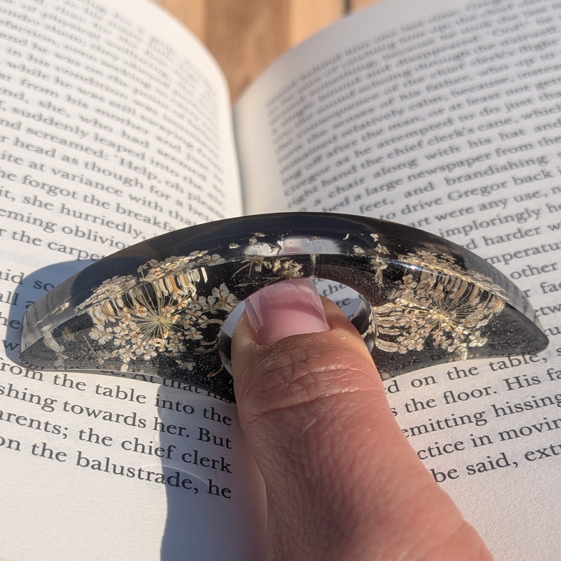 Handmade black resin page holder ring with Queen Anne's Lace – front view on wooden surface – EL-Creations