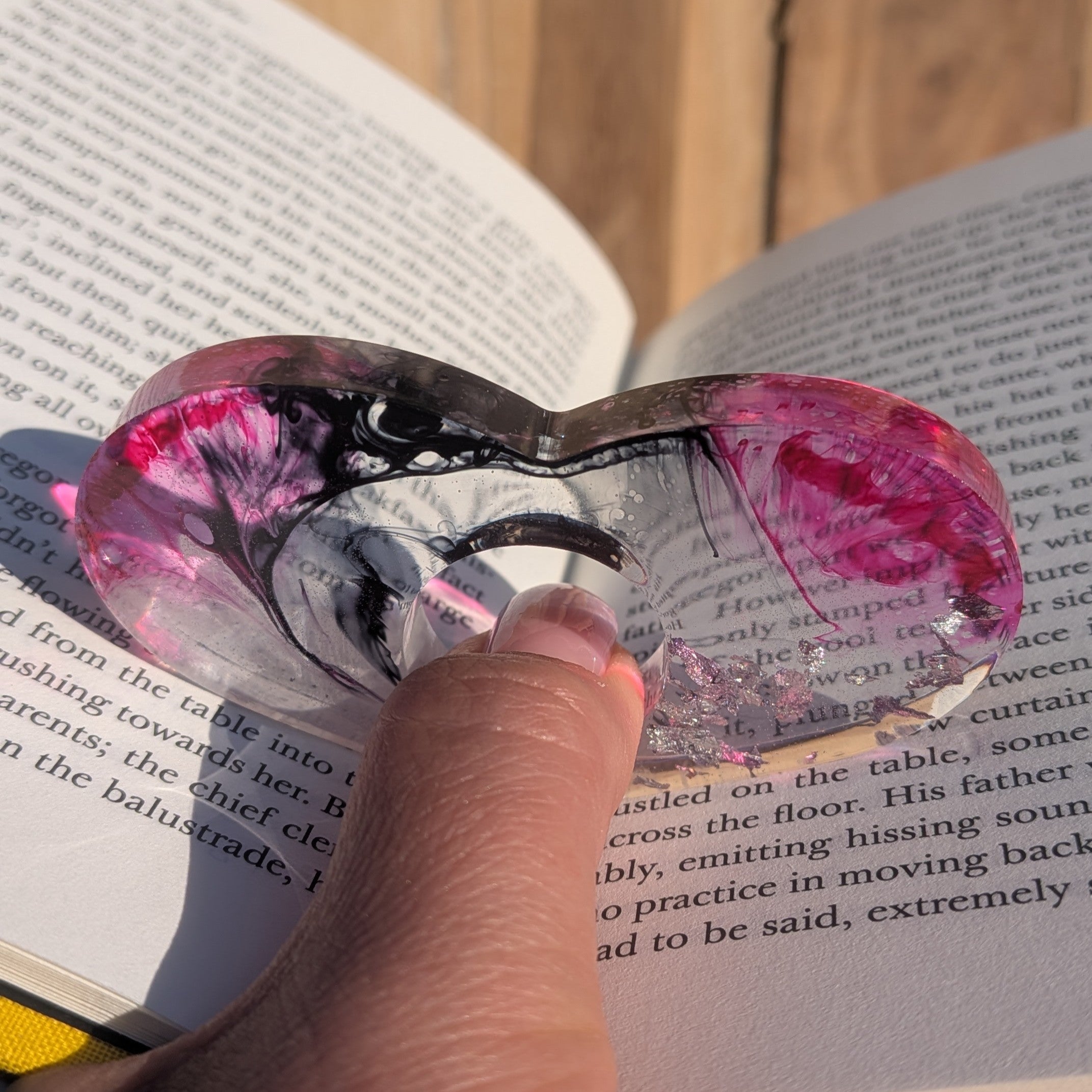 Large handmade resin book ring with silver flakes and crimson black gradient – angled view on sandy surface – EL-Creations