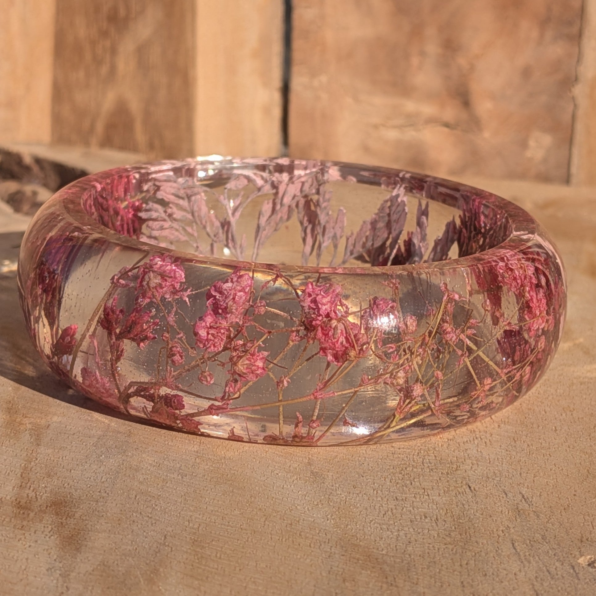 Handmade clear resin bangle with pink Baby's Breath worn on wrist – lifestyle shot on wooden background – EL-Creations