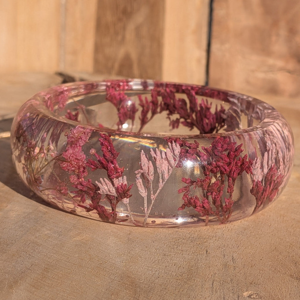 Clear resin botanical bangle with pink Baby's Breath and wild flowers – top view on sandy surface – EL-Creations