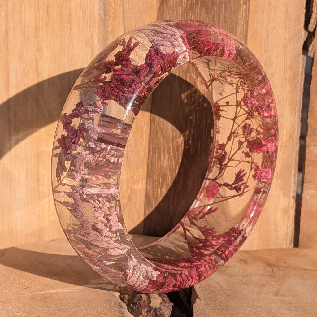 Handmade clear resin bangle with pink Baby's Breath – standing upright on wooden surface – EL-Creations