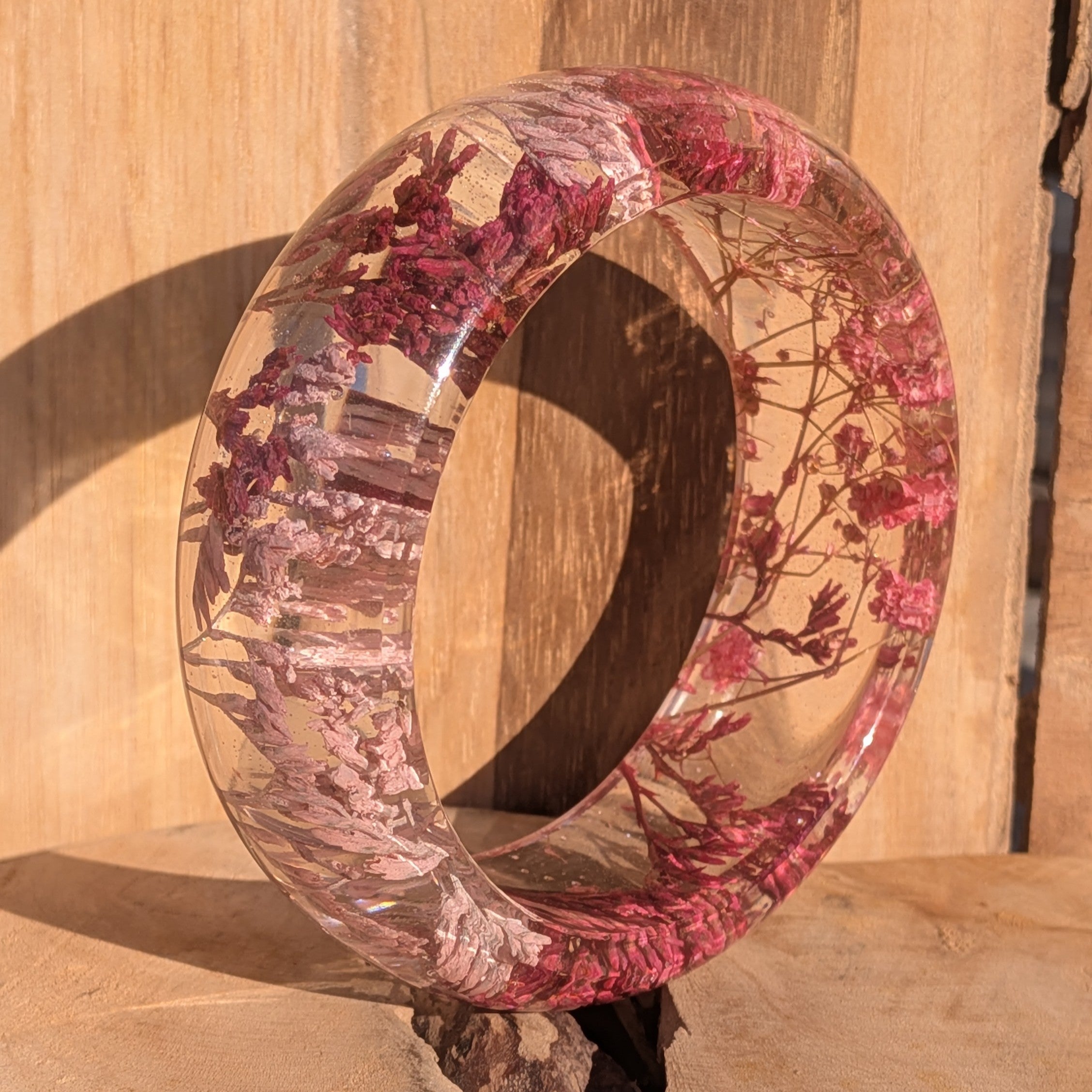 Handmade clear resin bangle with pink Baby's Breath – standing upright on wooden surface – EL-Creations