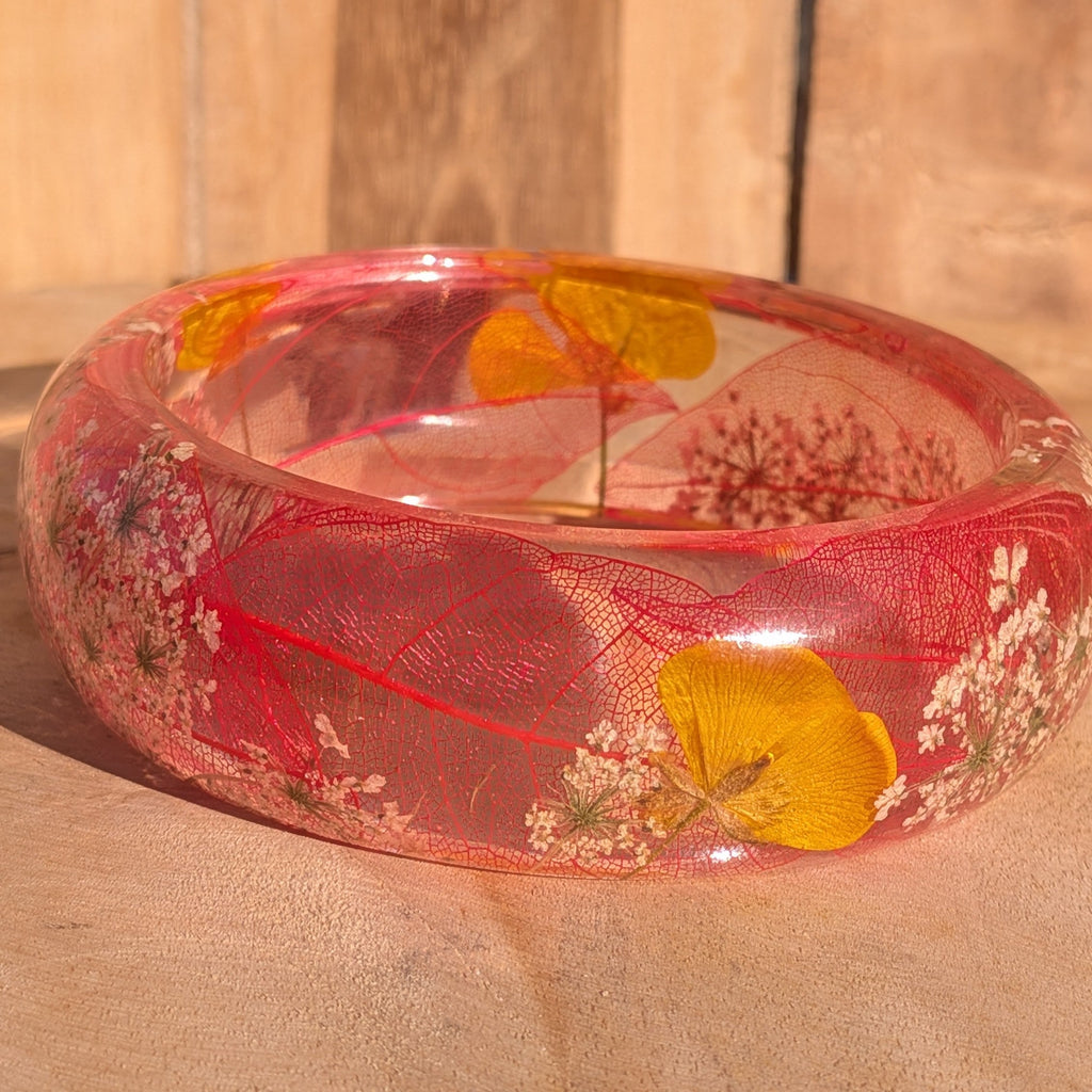 Clear resin botanical bangle with skeleton leaf and yellow wildflowers – angled view on wooden surface – EL-Creations