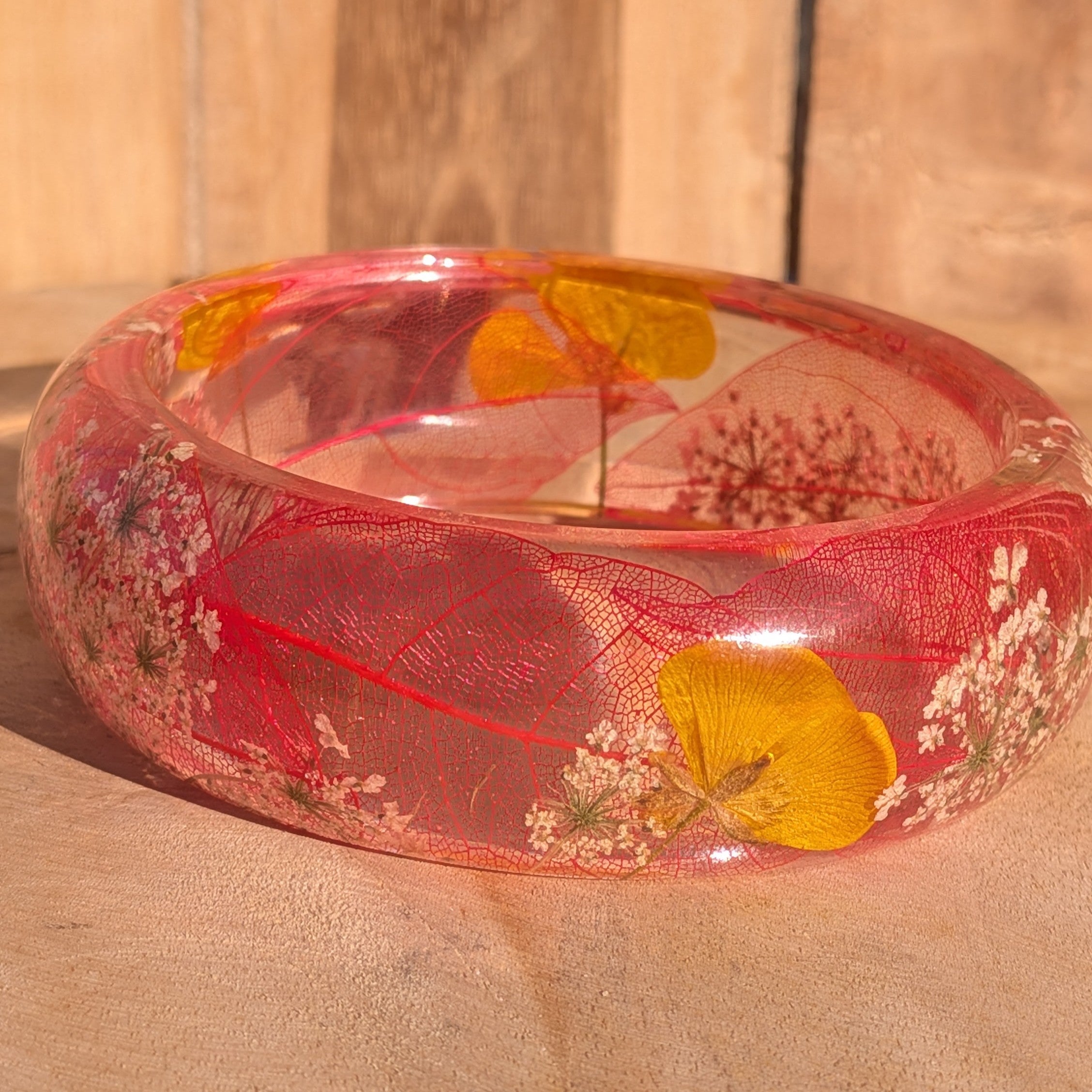 Clear resin botanical bangle with skeleton leaf and yellow wildflowers – angled view on wooden surface – EL-Creations