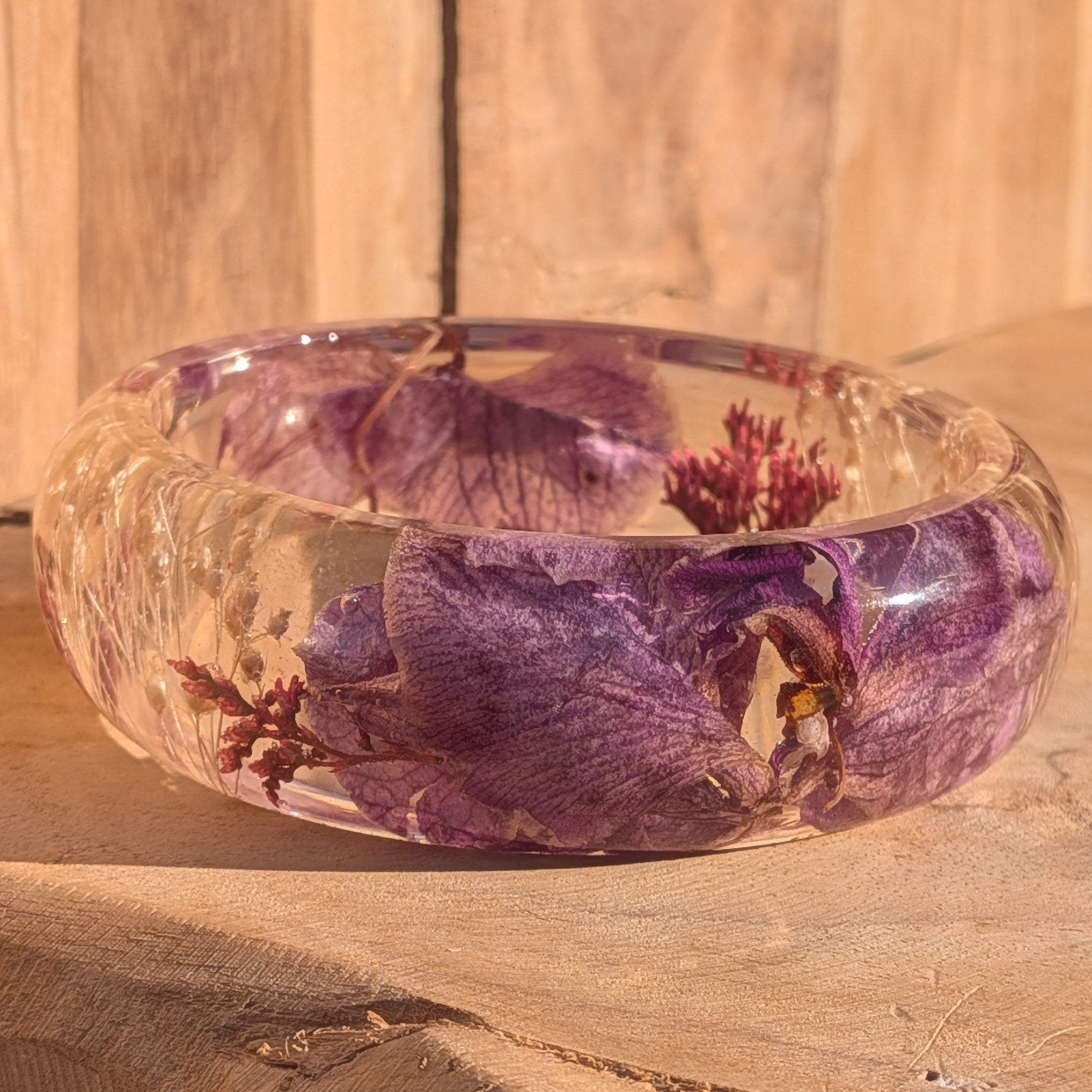 Clear resin botanical bangle with orchid petals and heather flowers – angled view on wooden surface – EL-Creations